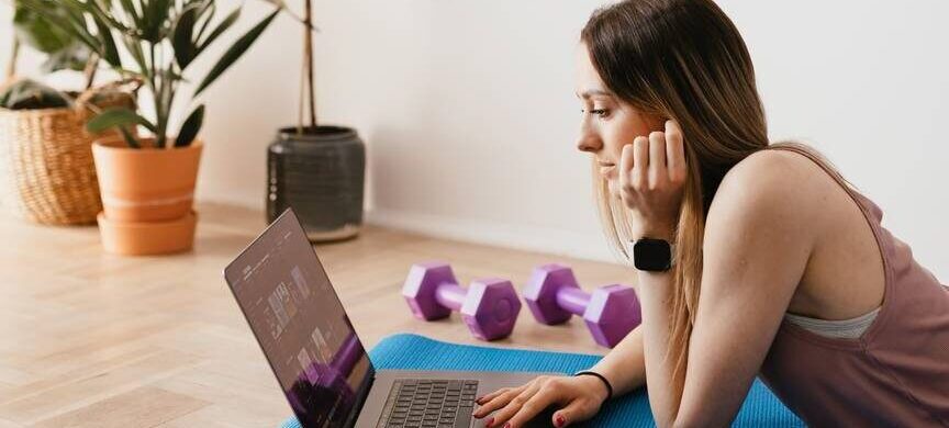 young woman browsing laptop and lying on mat