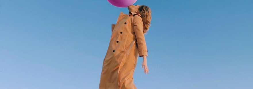 young female blowing huge balloon in sky